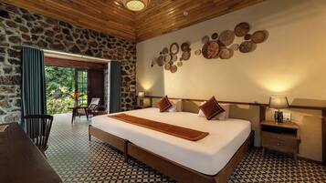 A spacious bedroom with a large bed, a stone wall, and a view of greenery.