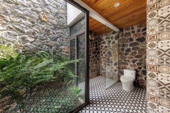 A bathroom with a stone wall, a wooden ceiling, and a patterned floor.