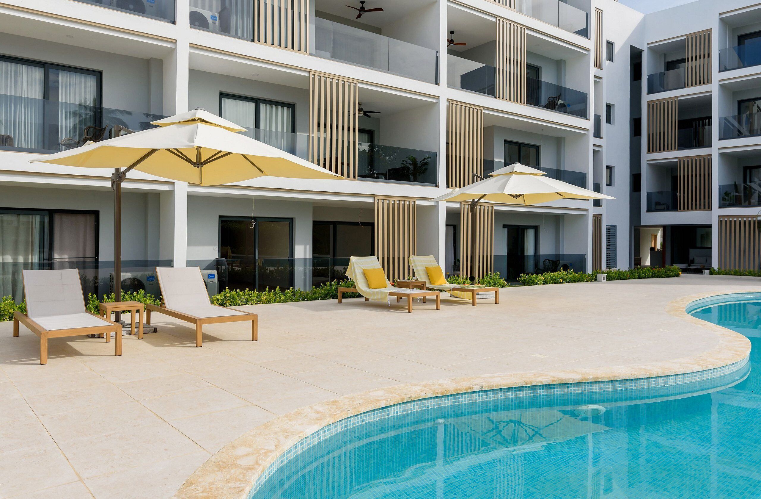 A modern hotel with a pool area, sun loungers, and umbrellas.