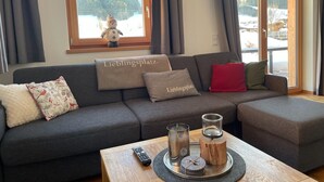 A modern living room with a grey sectional sofa, a wooden coffee table with a remote control, candles, and a tray. - Chalet in Alps Near Ski Lift & Slope (St. Ulrich Am Pillersee)
