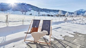 A wooden deck with two lounge chairs, one with a cushion and a blanket, and a banner with a mountain logo. - Chalet in Alps Near Ski Lift & Slope (St. Ulrich Am Pillersee)
