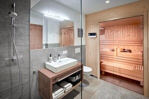 A modern bathroom with a glass-enclosed shower, a wooden vanity with a sink, and a sauna area. - Chalet in Alps Near Ski Lift & Slope (St. Ulrich Am Pillersee)