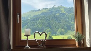 A window with a view of a green landscape and a cross on a hill. - Chalet in Alps Near Ski Lift & Slope (St. Ulrich Am Pillersee)