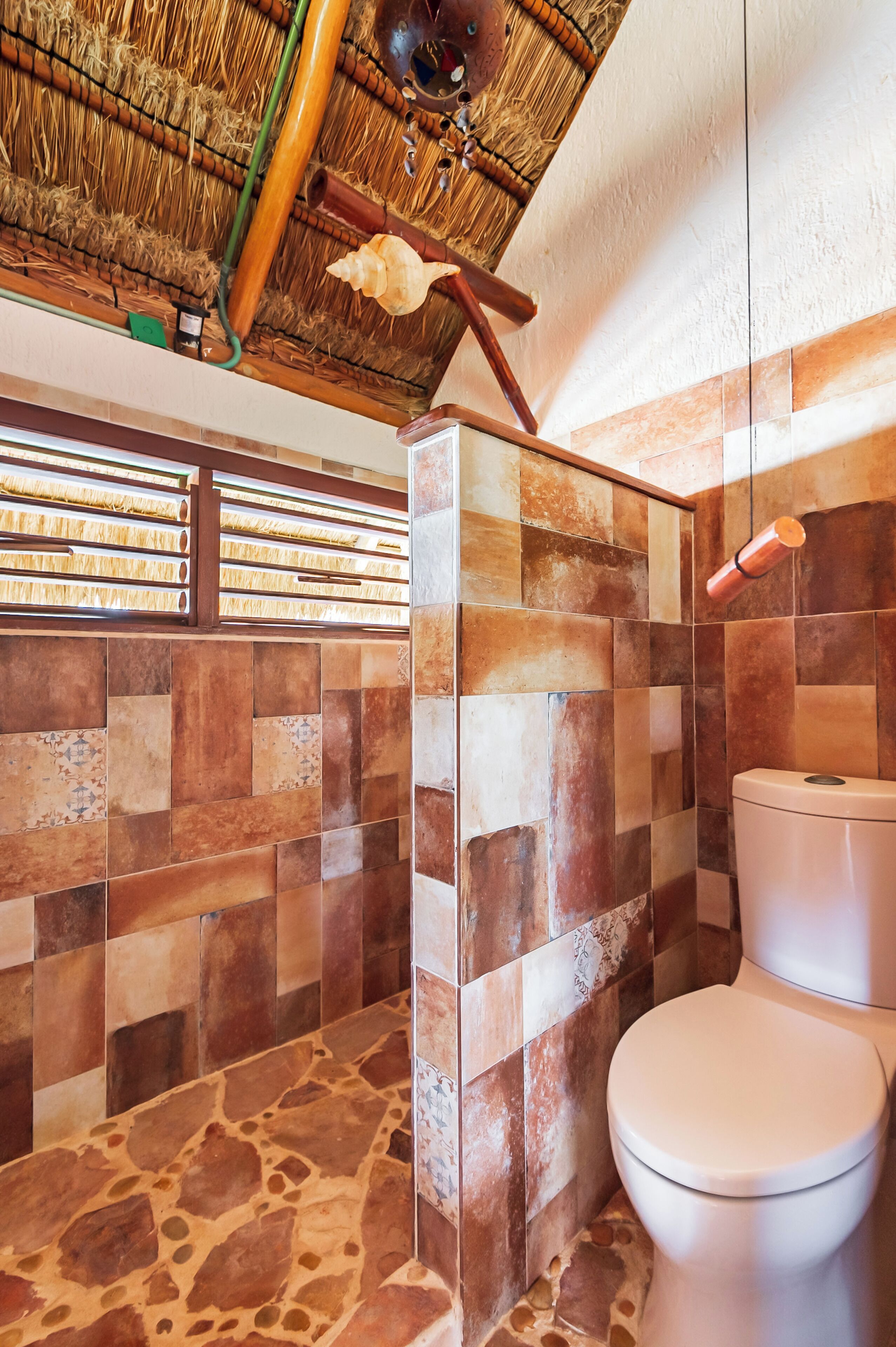 Une salle de bain avec un sol en pierre, des toilettes blanches et un espace douche séparé par une paroi en verre.