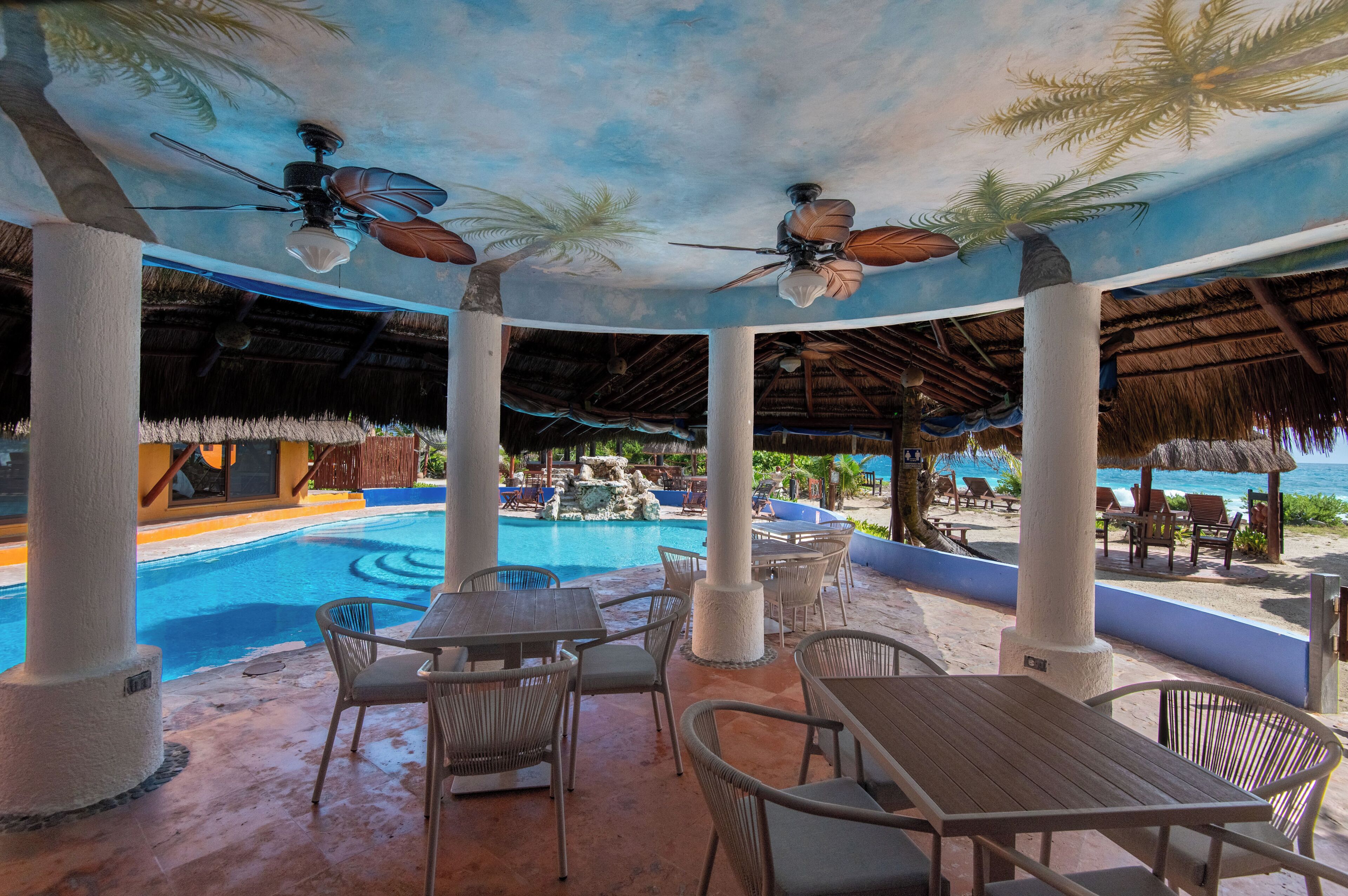 A covered outdoor area with a pool, seating, and ceiling fans.