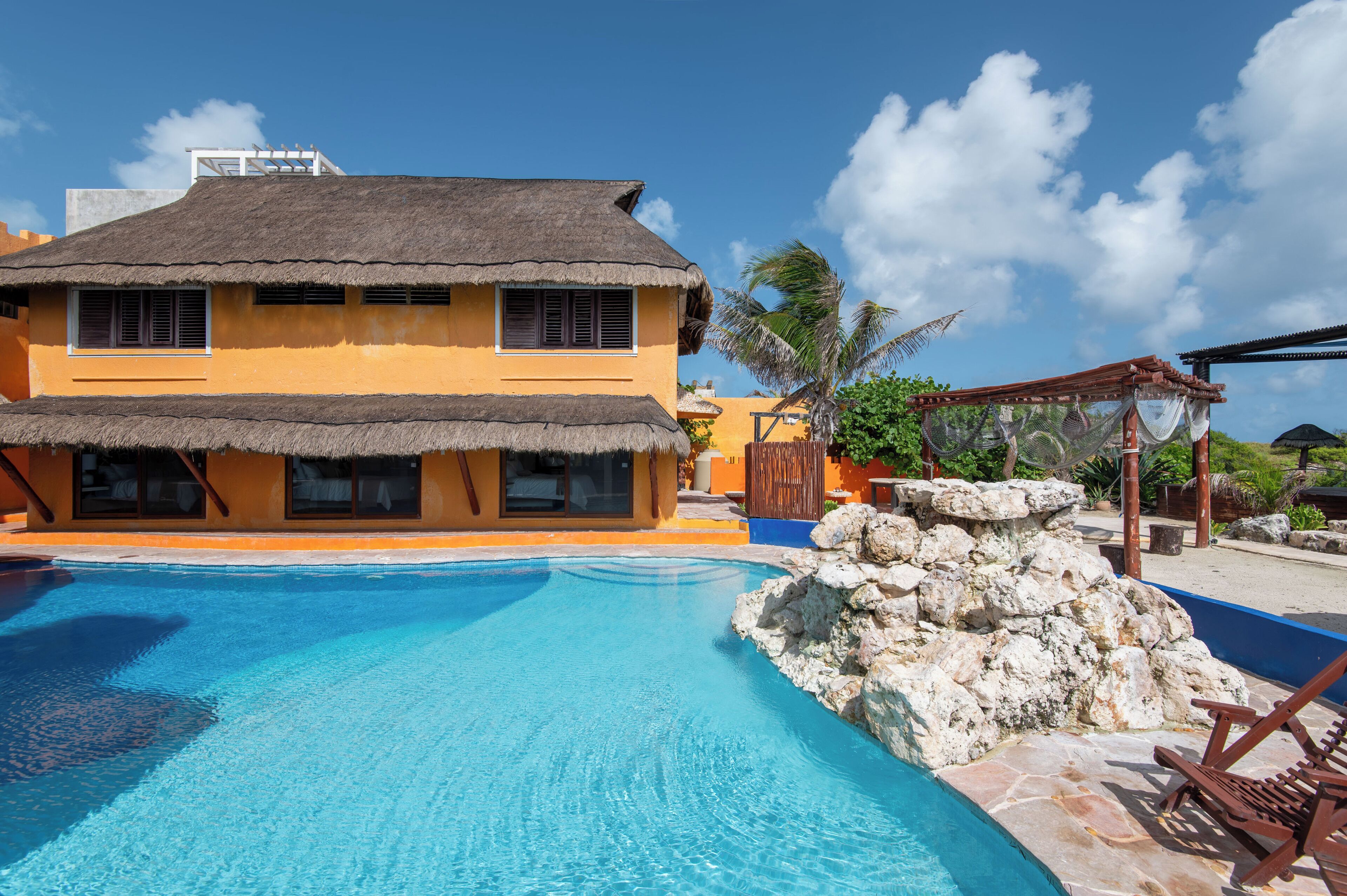 Un hôtel doté d’une piscine, d’un bâtiment à toit de chaume et d’une formation rocheuse.