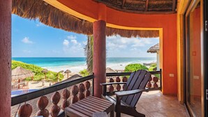 Un balcon avec vue sur l’océan, des chaises en bois et un toit de chaume.
