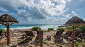 Une plage avec des chaises longues en bois et des parasols en chaume, donnant sur l’océan.