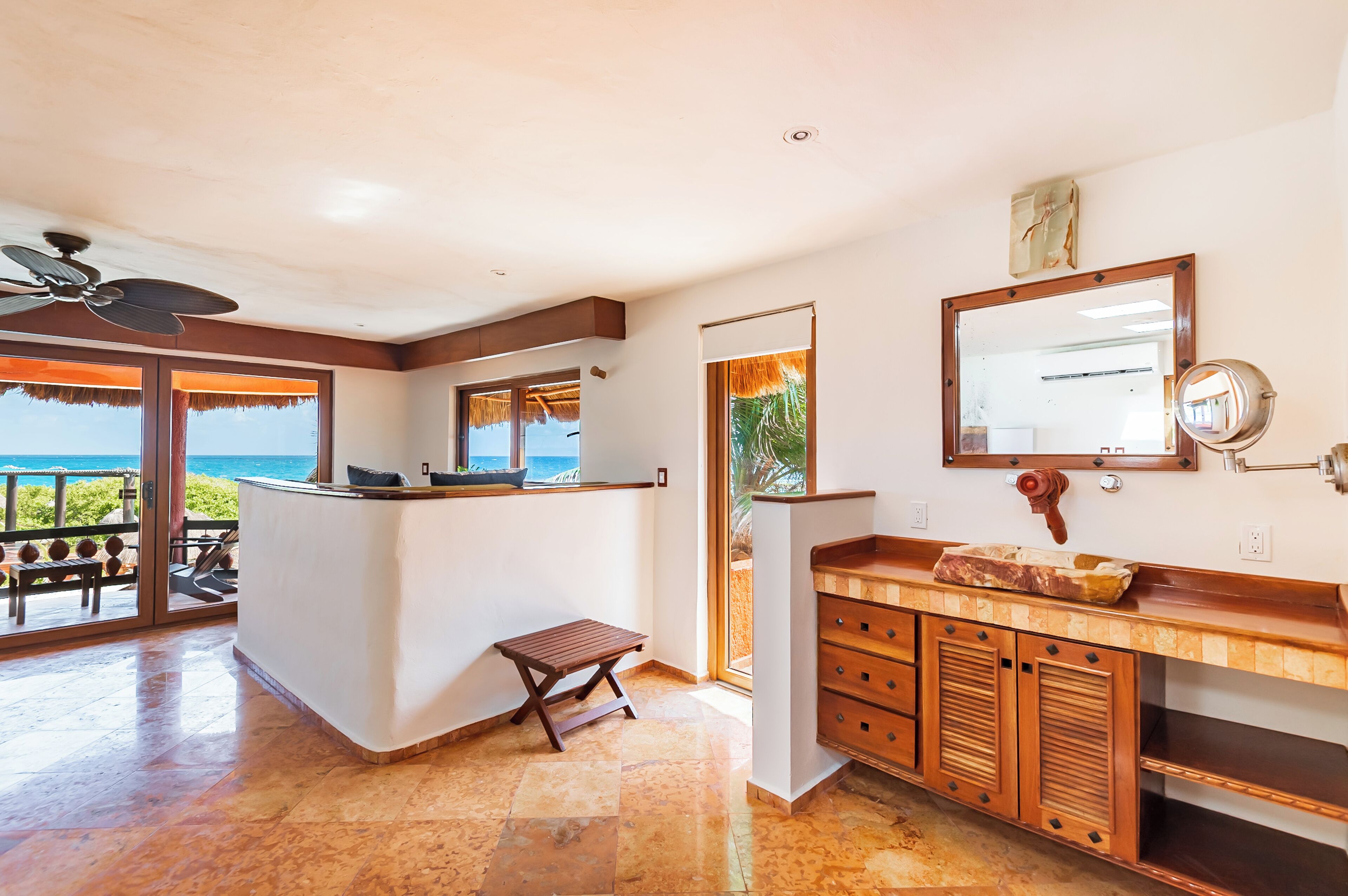 A modern kitchen with a large island, a wooden bench, and a view of the ocean.