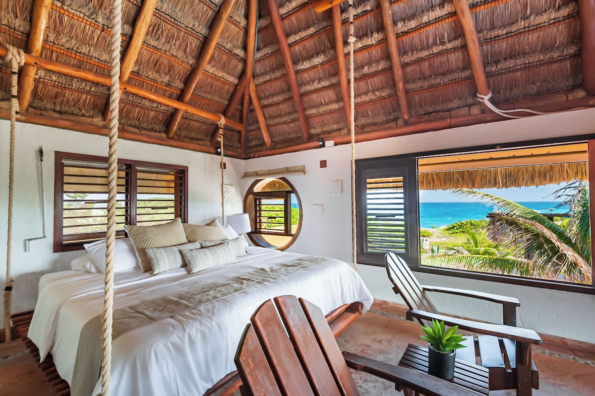 A room with a bed, a chair, a potted plant, and a view of the ocean.