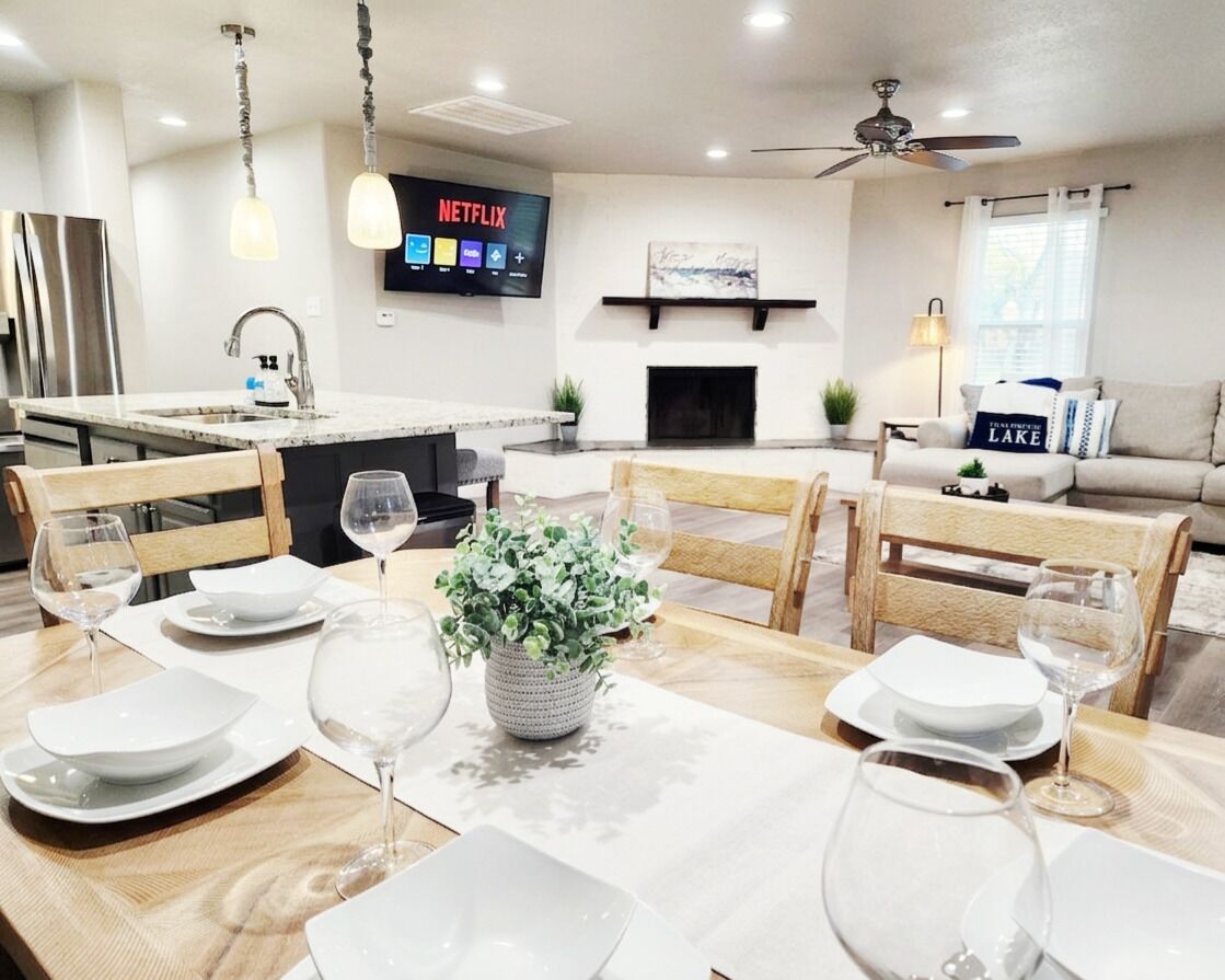 A modern kitchen with a built-in island, a dining area with a wooden table set for four, and a living room with a sofa and a fireplace.