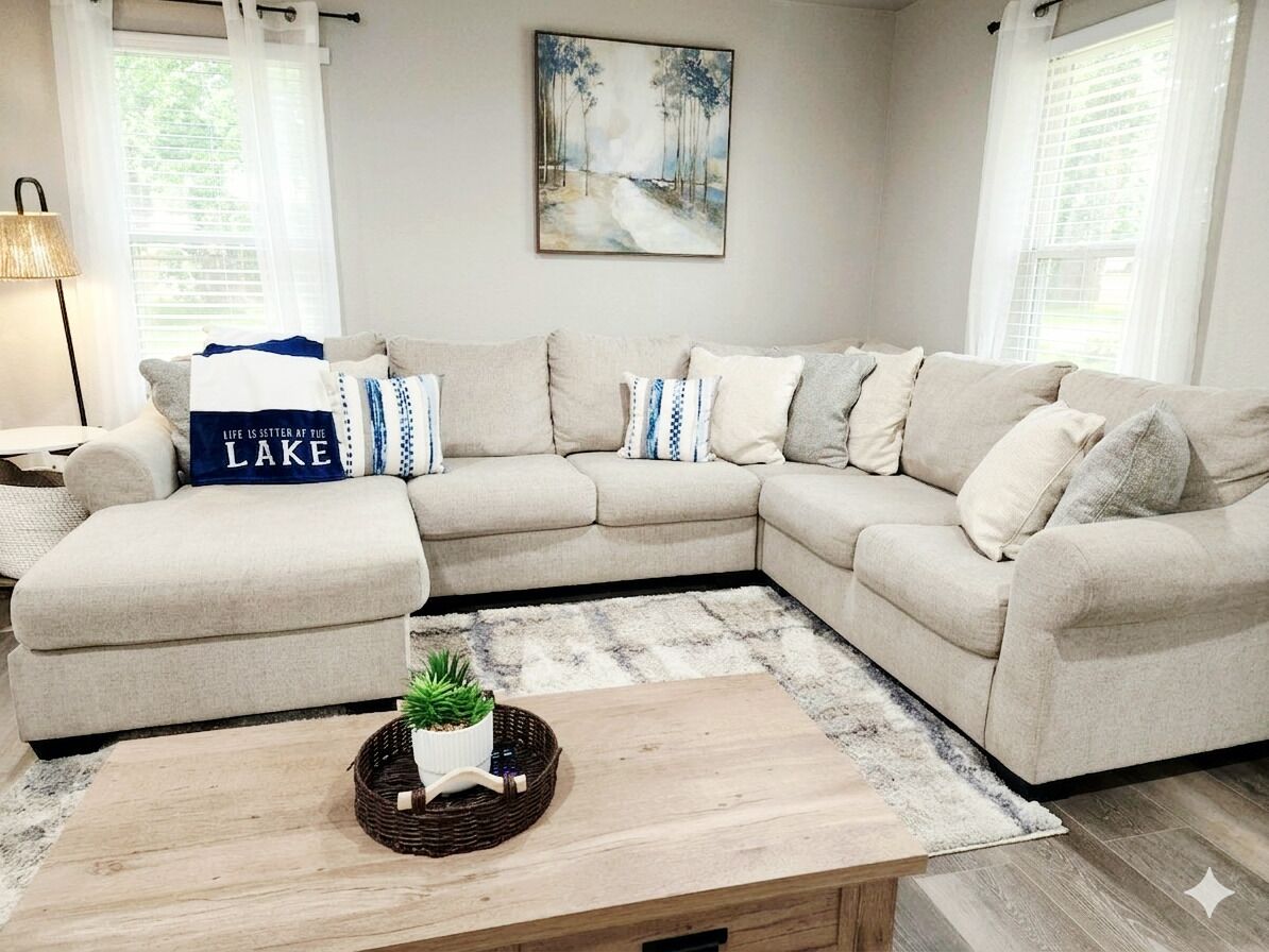 A L-shaped beige sofa with a matching ottoman, a small wooden coffee table with a plant, and a painting on the wall.