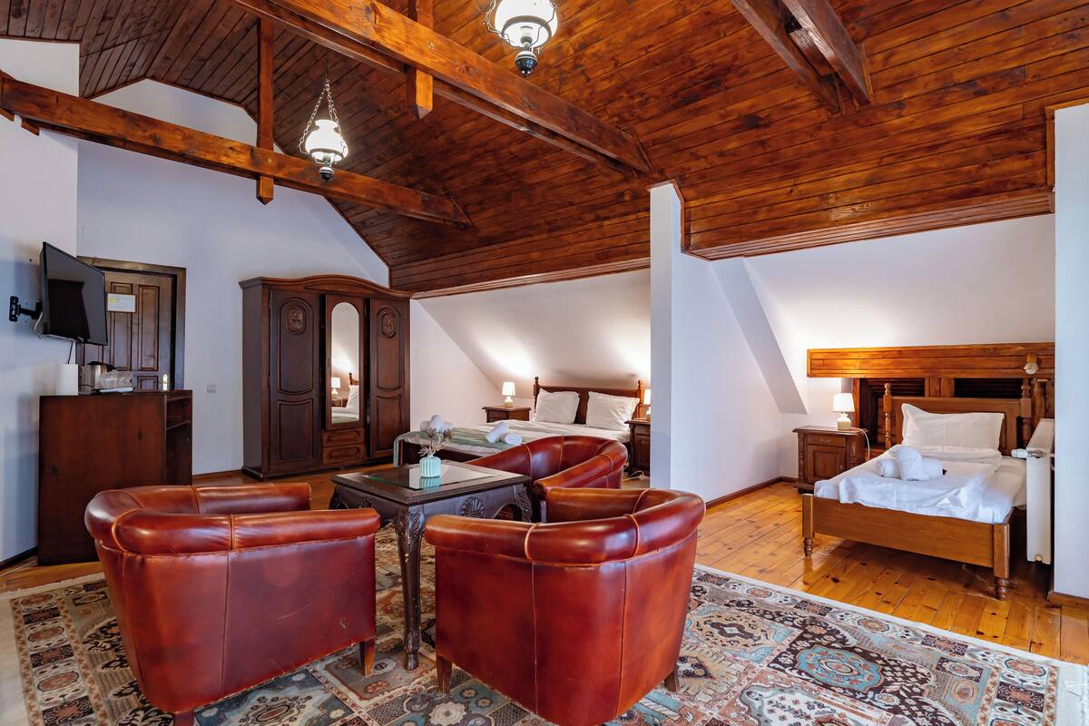 A cozy attic bedroom with a wooden ceiling, a large bed, a desk with a chair, a TV, and a wardrobe.