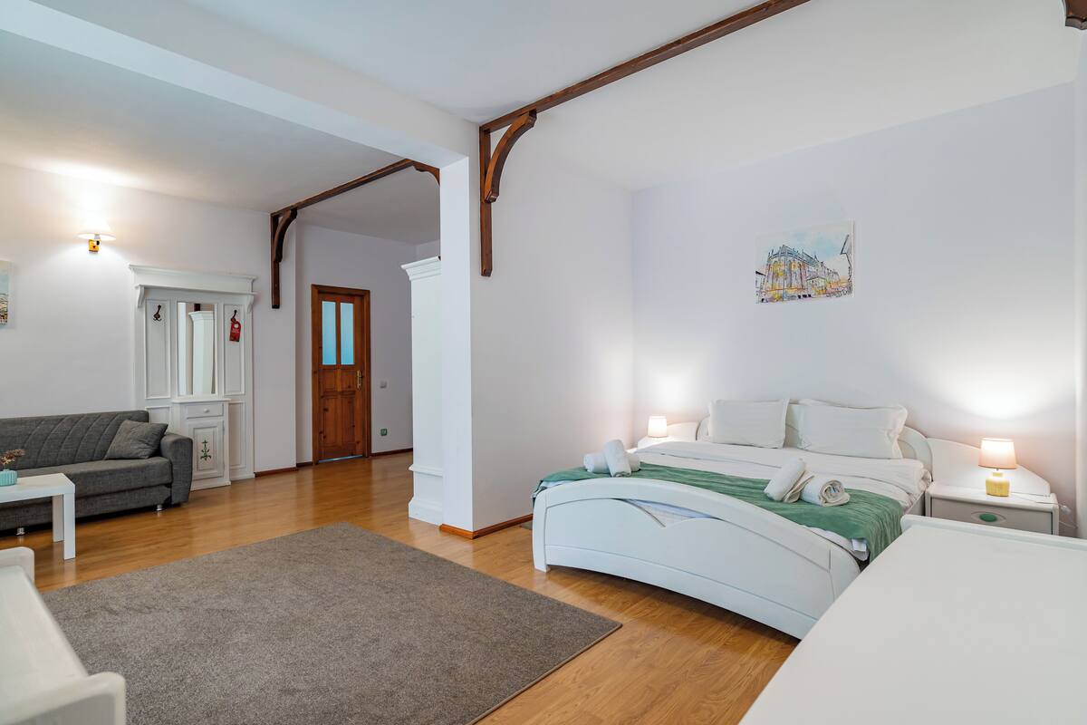 A bedroom with a bed, bedside tables, a nightstand, a sofa, a coffee table, and a door leading to another room.