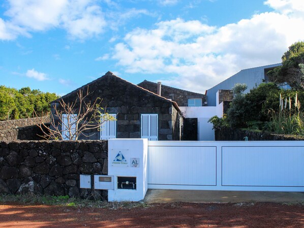 A stone building with a white exterior, a stone wall, and a fenced area. - Atlantis Breeze (Madalena)
