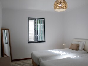 A bedroom with two beds, a window, a mirror, and a hanging light fixture. - Atlantis Breeze (Madalena)