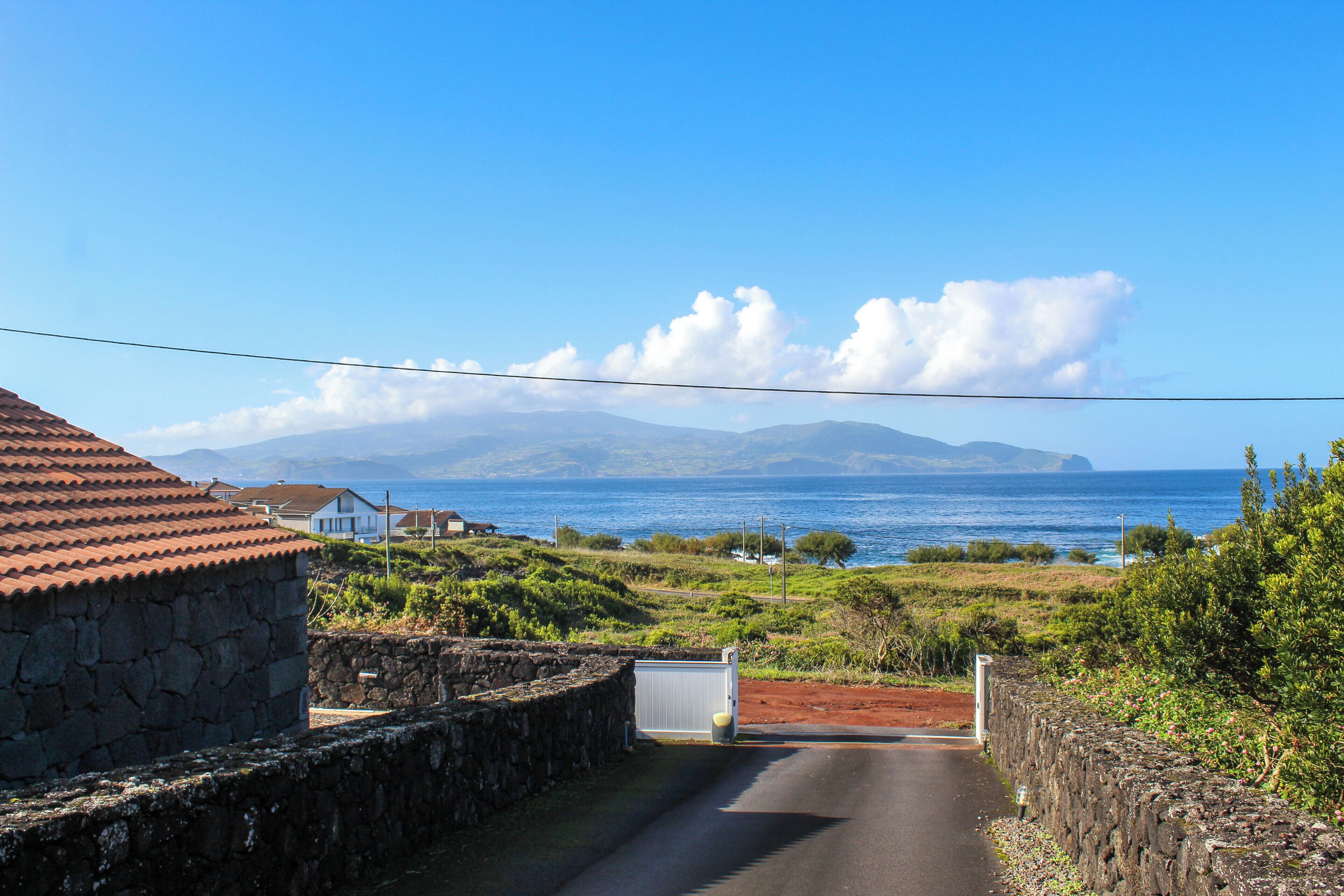 Eine Küstenstraße mit Steinmauern und freiem Blick auf das Meer und die entfernten Berge.
