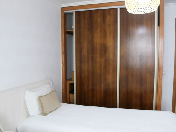 A bedroom with a bed, a wooden wardrobe, and a hanging light fixture. - Atlantis Breeze (Madalena)