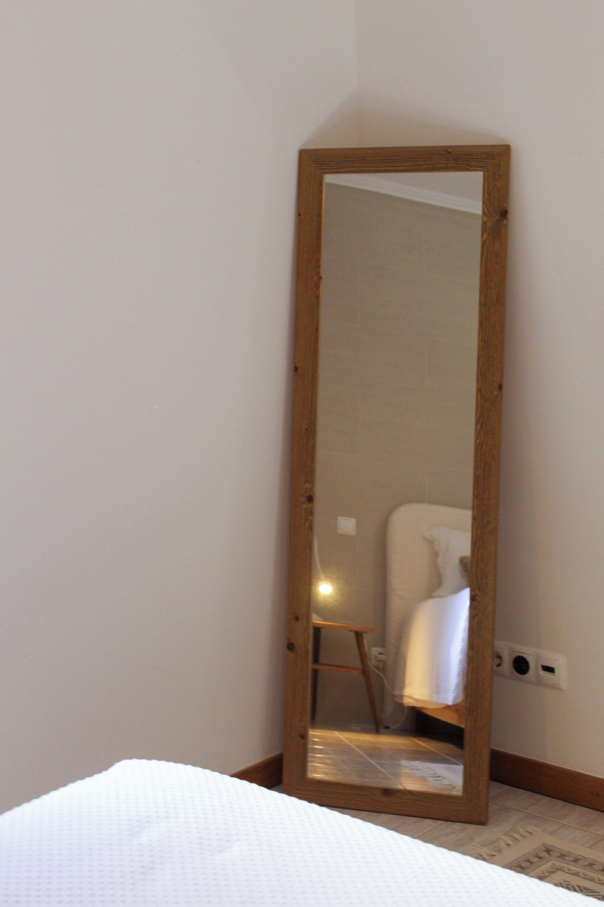 Ein Zimmer mit einem großen Spiegel mit Holzrahmen, einem weißen Bett und einem kleinen Stuhl.