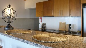 Een keuken met granieten aanrechtbladen, houten kastjes, een ingebouwde kookplaat en een hangende lamp.