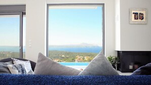 Un soggiorno con un'ampia finestra che si affaccia su un paesaggio costiero e una piscina.