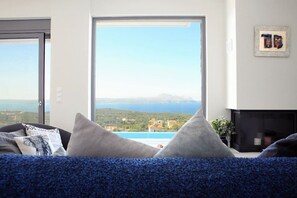 A living room with a large window offering a view of a coastal landscape and a pool.
