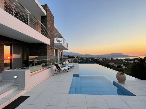 A modern house with a rooftop pool, a balcony with lounge chairs, and a scenic view of the landscape.