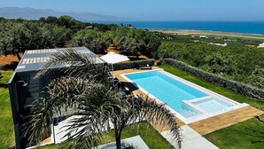Une maison moderne dotée d’une piscine, entourée d’une végétation luxuriante et offrant une vue sur l’océan.