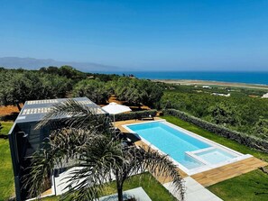A modern house with a swimming pool, surrounded by lush greenery and a view of the ocean.