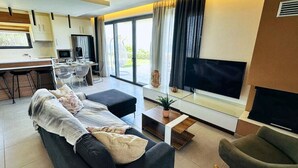 Un salon moderne avec un canapé, une table basse et un téléviseur. Il y a également un coin cuisine avec un réfrigérateur et une table à manger.