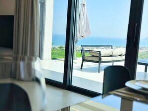 A modern room with a large window overlooking a patio with a bench and umbrella. - Skyline Ocean - 20PL 8BD 6BA, 3min to the beach (GR9M+6V5 Platanias, Greece)