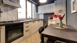 Een moderne keuken met een gasfornuis, oven en witte kasten. Er staat een eettafel met stoelen en een bloemenvaas.