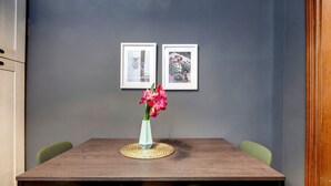 Een eettafel met een bloemenvaas, twee ingelijste foto's aan de muur en groene stoelen.