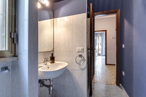 Uma casa de banho com lavatório branco, espelho e paredes em azulejo.
