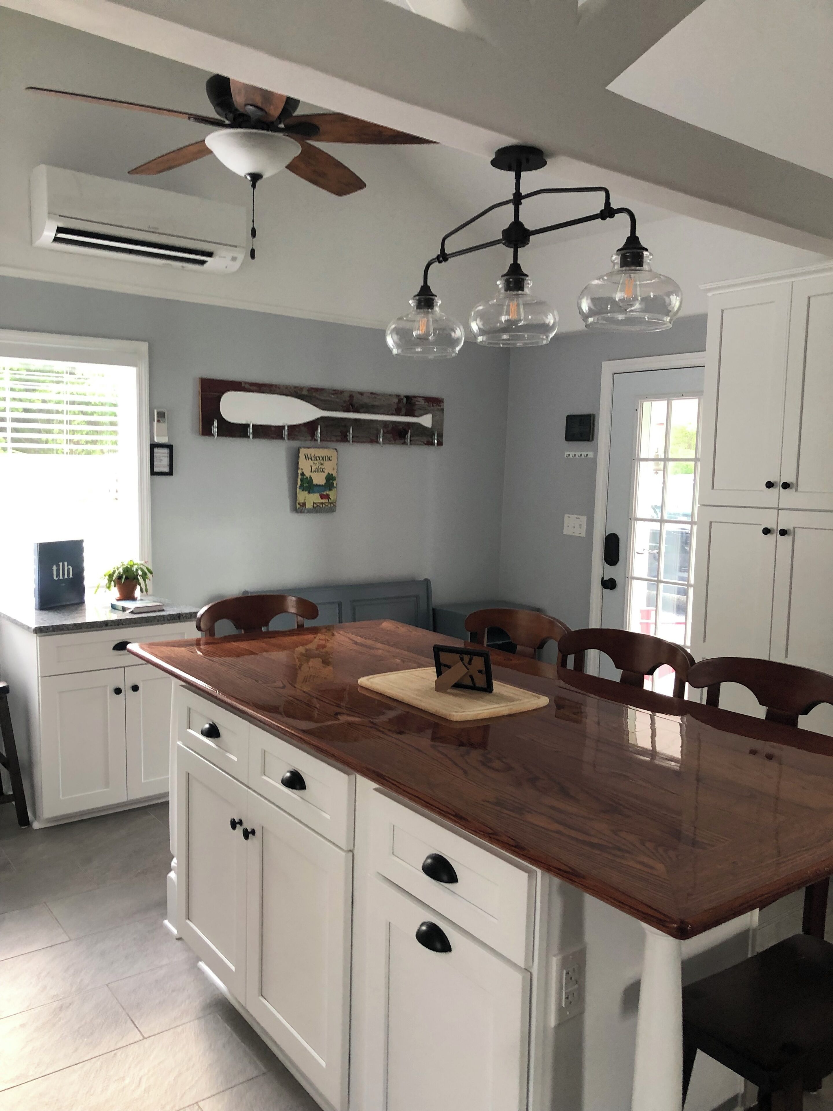A kitchen with a wooden island, white cabinetry, a ceiling fan, and pendant lights.