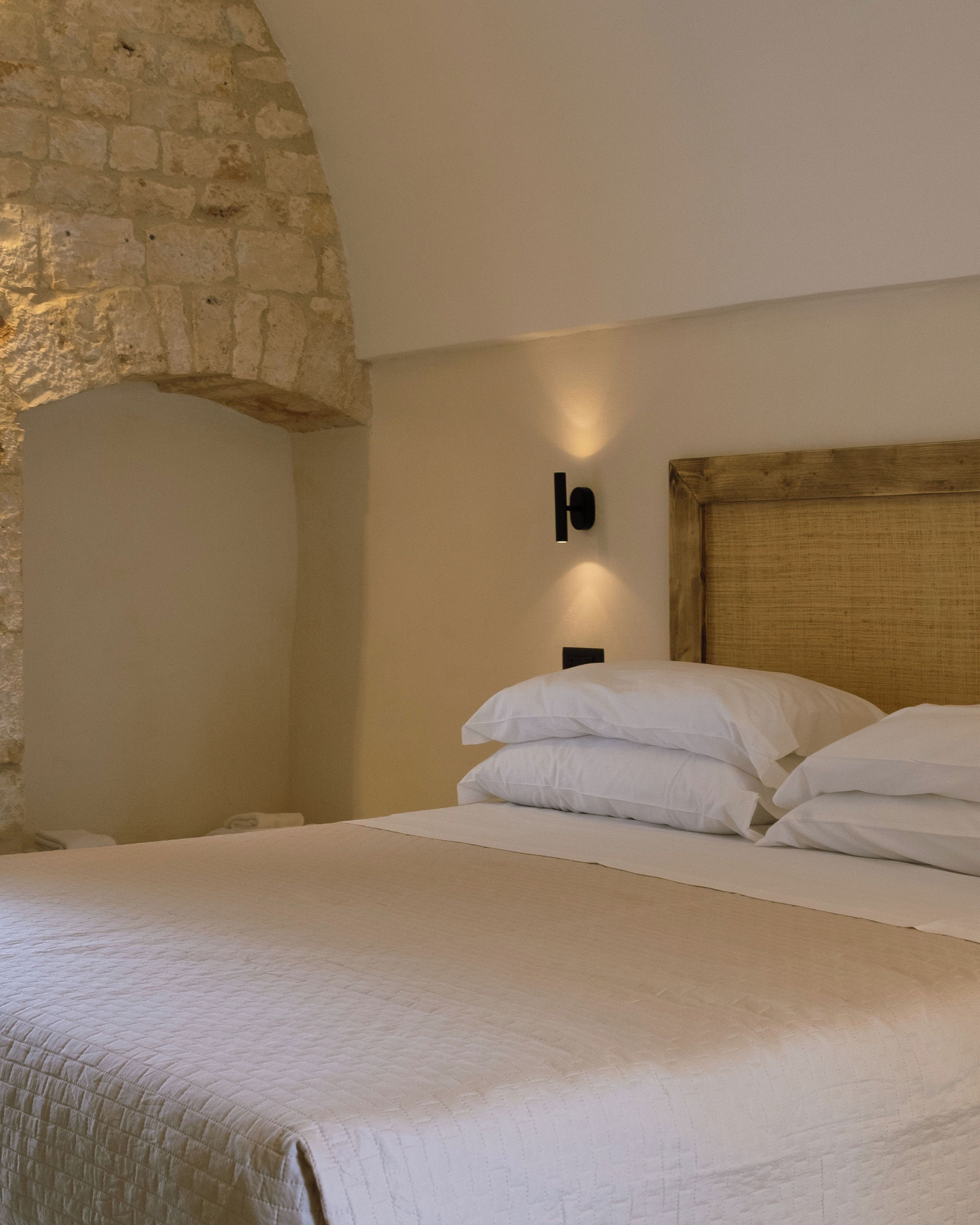 A bed with white linens in a room with a stone wall and a wooden headboard.