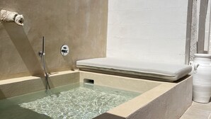 Un área de spa con una bañera de hidromasaje, una ducha y una pared blanca.