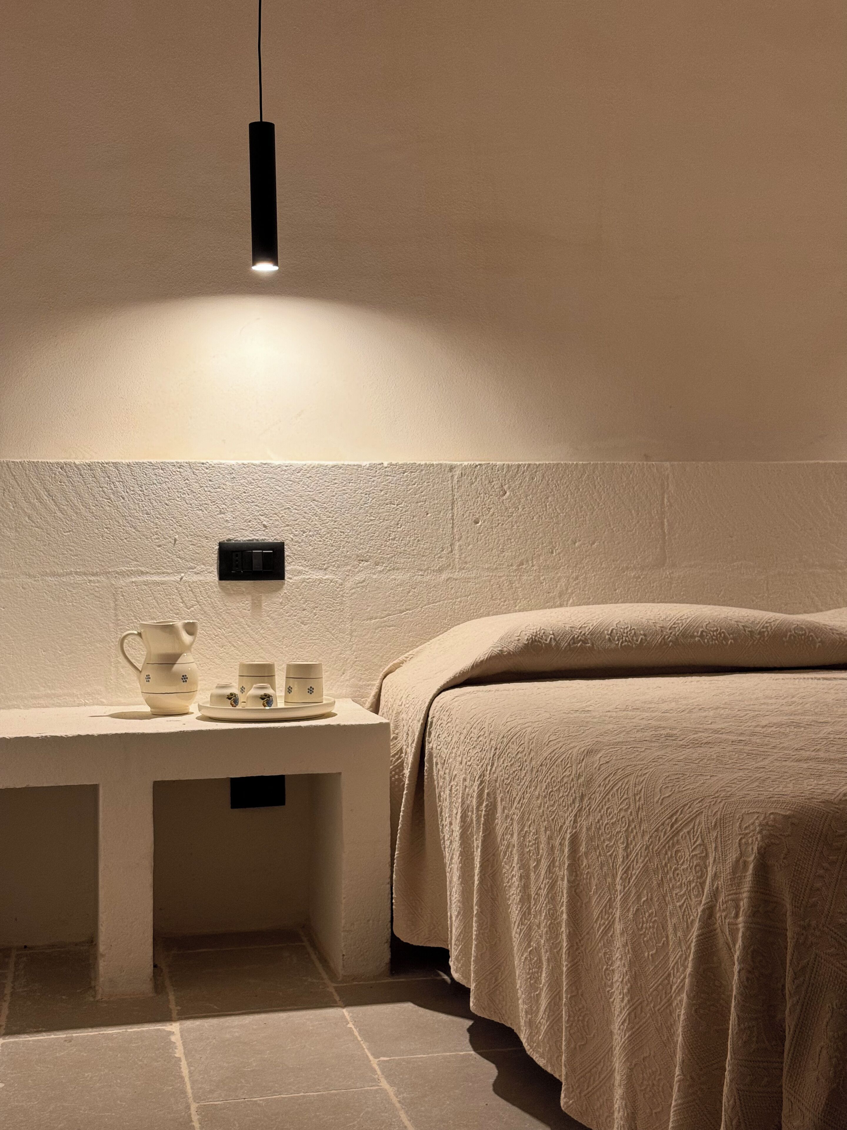 A bedroom with a bed, bedside table, and a hanging light fixture.