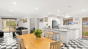 A modern kitchen with white cabinets, a central island, and a dining area with a checkered floor. - Prez Cote La Plaz - Pet Friendly -1 Min Walk to Beach (Callala Bay)