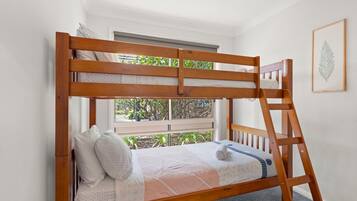 Un letto a castello con una scaletta, biancheria bianca e una finestra con vista sul verde.