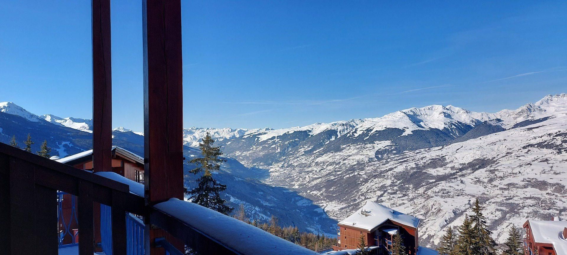 A mountain cabin with a clear view of snow-covered peaks and a forested valley.
