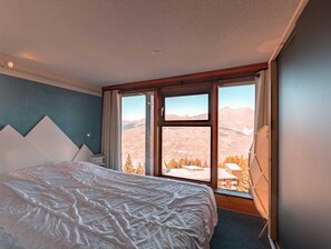 Ein Schlafzimmer mit Bett, Fenster und Blick auf die Berge sowie einem hölzernen Kopfteil.