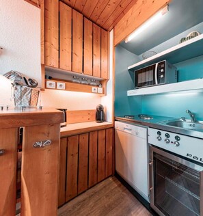 A compact kitchen with wooden cabinets, a built-in microwave, a stove, and a dishwasher.