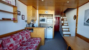 A compact kitchen with a microwave, refrigerator, and wooden cabinets. A red and white patterned sofa is in the foreground, and a painting of a snowy scene is on the wall. - 50m from ski slopes, 3rd floor, tv, 33m², Les Arcs (Les Arcs)