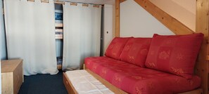 Een kamer met een houten bed, rode beddengoed, een houten garderobe en een wit gordijn.