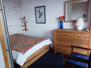 Een slaapkamer met een houten bed, een kaptafel, een spiegel en een ingelijst poster aan de muur.