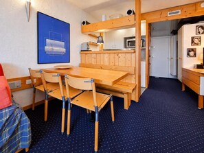 Een compacte kamer met een eettafel, stoelen, een kitchenette en een bed met een rode deken.