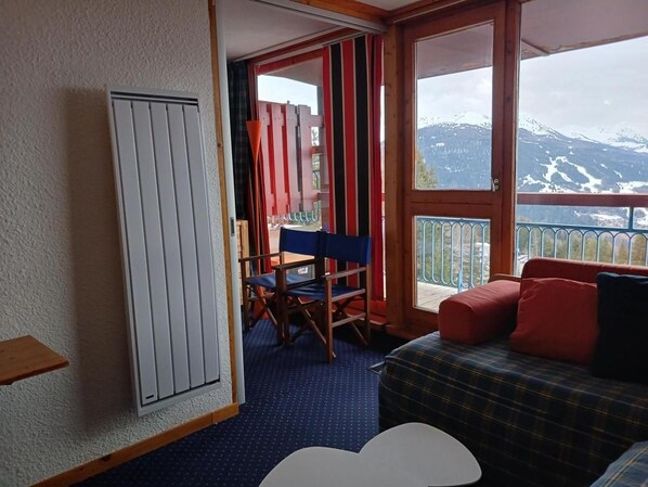 Een kamer met een bed, een tafel, een stoel en een raam met uitzicht op de bergen.