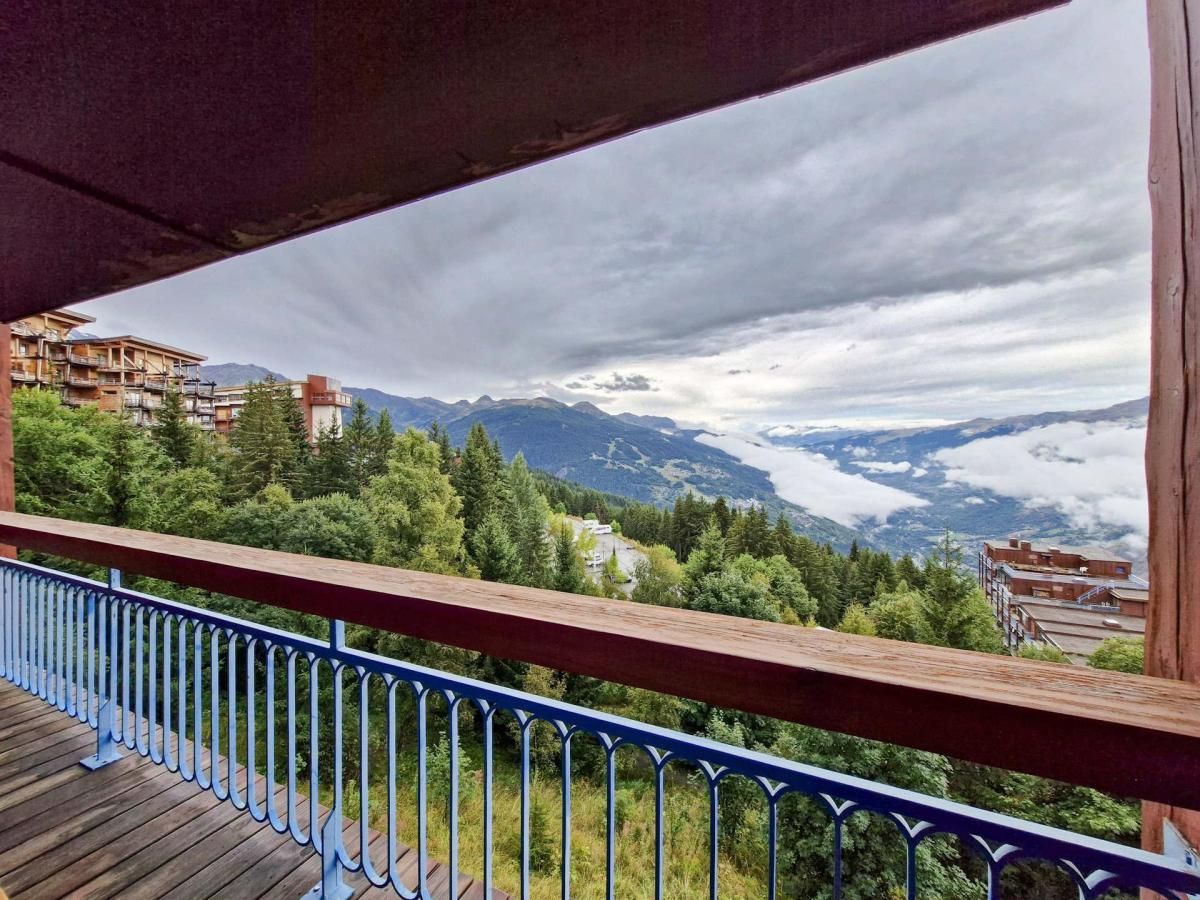 A balcony with a view of a mountainous landscape, including buildings and trees.