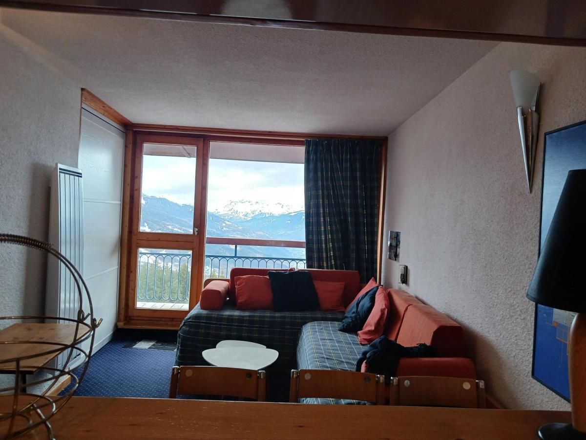 A compact room with a bed, a small table, and a window with a mountain view.